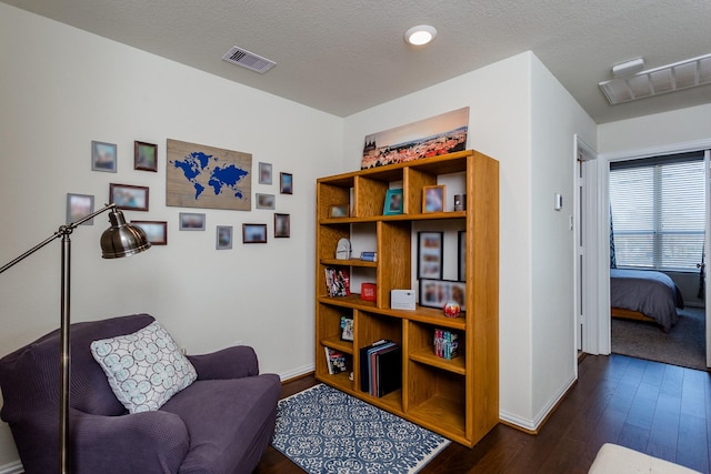 living area featuring a textured ceiling, visible vents, dark wood finished floors, and baseboards