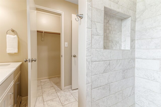 full bath featuring a walk in closet, tiled shower, marble finish floor, and vanity