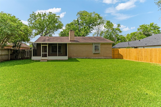 back of house with a chimney, a fenced backyard, a sunroom, and a lawn