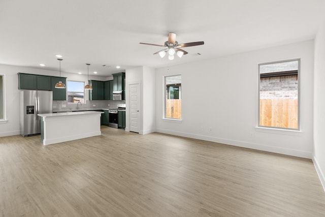unfurnished living room with a wealth of natural light, light wood-type flooring, baseboards, and a sink