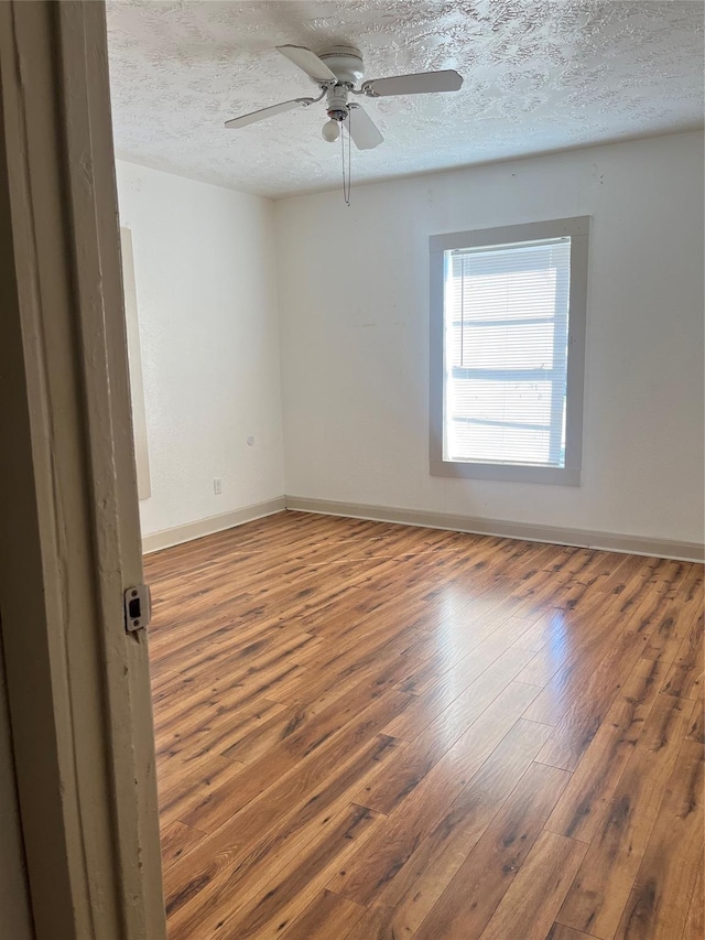 empty room with a textured ceiling, ceiling fan, hardwood / wood-style flooring, and baseboards