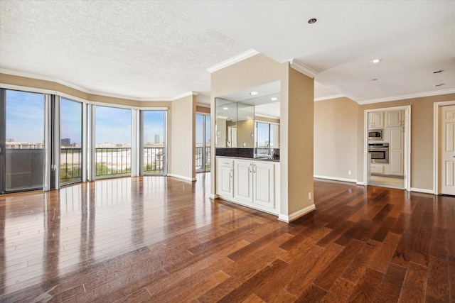 unfurnished living room featuring a textured ceiling, wood finished floors, ornamental molding, and baseboards