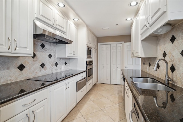 kitchen with dark stone countertops, white cabinets, a sink, appliances with stainless steel finishes, and under cabinet range hood