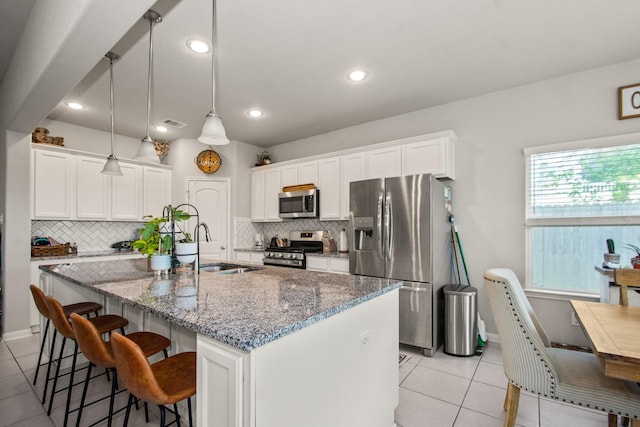 kitchen with light tile patterned floors, stainless steel appliances, backsplash, a sink, and a center island with sink