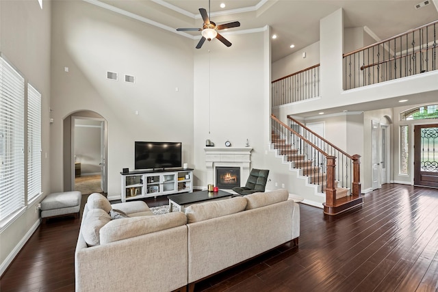 27803 Indigo Pointe Ln, Katy, TX 77494 - living room featuring a glass covered fireplace, a towering ceiling, ceiling fan, dark wood-style floors, and arched walkways