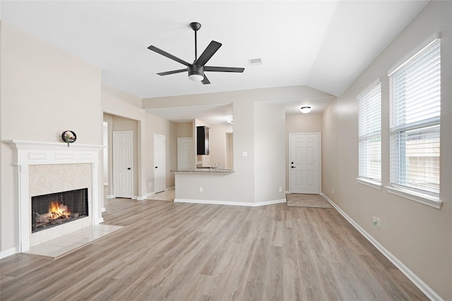 unfurnished living room featuring ceiling fan, visible vents, a tiled fireplace, lofted ceiling, and light wood-style floors