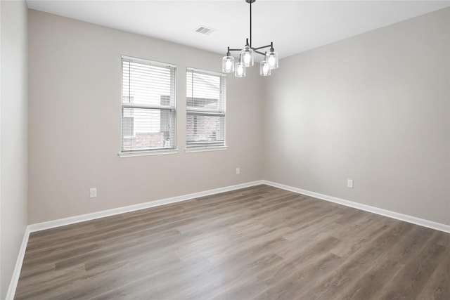 unfurnished room with baseboards, a notable chandelier, visible vents, and wood finished floors