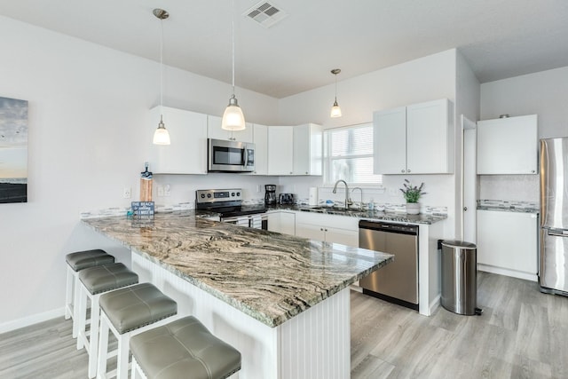 kitchen featuring a sink, appliances with stainless steel finishes, visible vents, light wood-style floors, and a peninsula