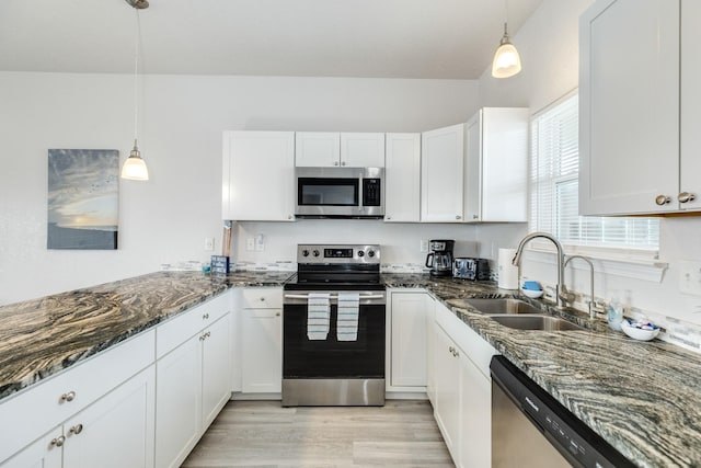 kitchen featuring dark stone countertops, stainless steel appliances, a sink, white cabinetry, and light wood-type flooring