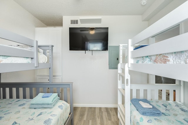 bedroom featuring visible vents, electric panel, wood finished floors, and baseboards