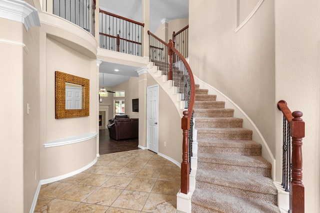 staircase featuring baseboards, stone finish floor, a high ceiling, and a warm lit fireplace