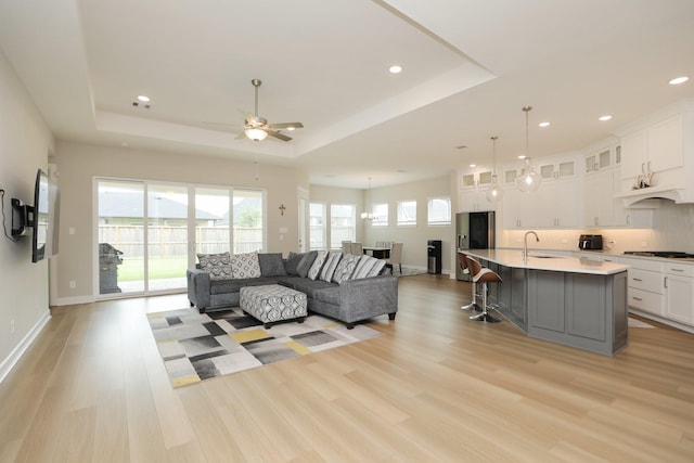 living area featuring ceiling fan, a healthy amount of sunlight, a raised ceiling, and light wood-type flooring