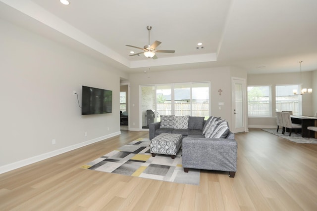 living room with baseboards, a raised ceiling, a healthy amount of sunlight, and light wood finished floors