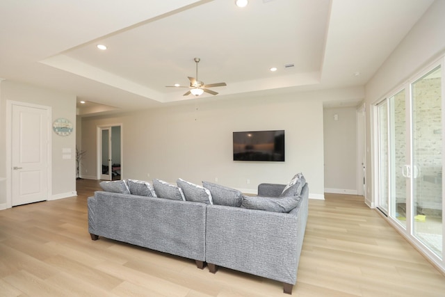 living area with a wealth of natural light, a raised ceiling, and light wood-style flooring