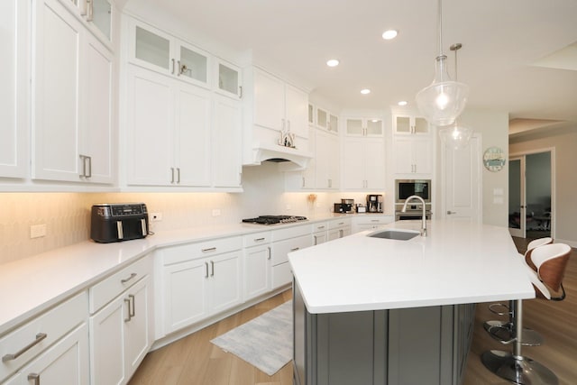 kitchen featuring a breakfast bar area, a sink, light wood-style floors, built in microwave, and gas stovetop