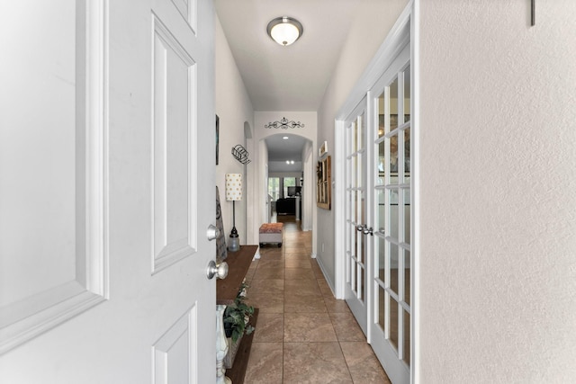 corridor with arched walkways, tile patterned flooring, and french doors
