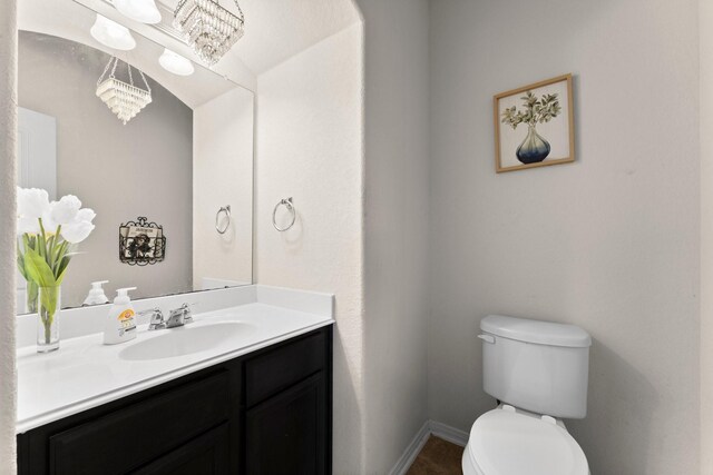 bathroom with toilet, an inviting chandelier, vanity, and baseboards