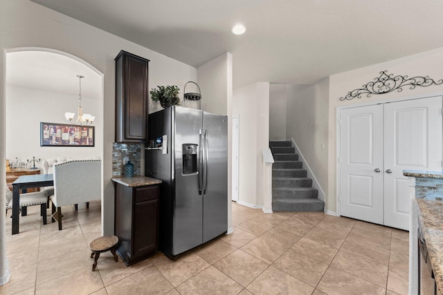kitchen featuring light stone countertops, arched walkways, an inviting chandelier, light tile patterned floors, and stainless steel fridge
