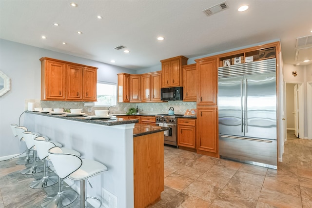 kitchen featuring visible vents, high end appliances, and brown cabinetry