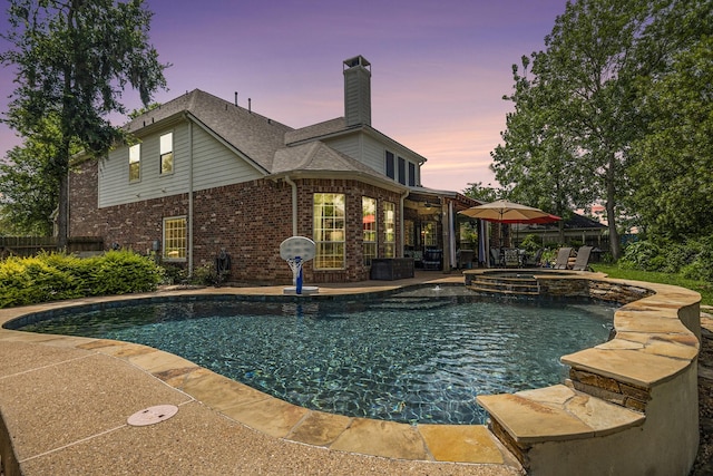 pool at dusk with a pool with connected hot tub and a patio area