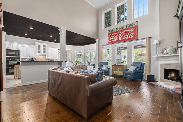 living area featuring crown molding, dark wood-style floors, decorative columns, a fireplace, and a towering ceiling