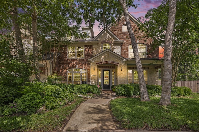 english style home featuring brick siding, stone siding, and fence