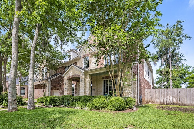 view of front of home with a front lawn, stone siding, brick siding, and fence