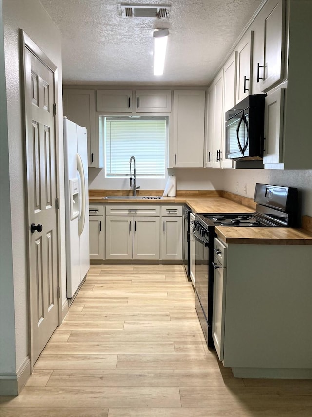 1402 Firwood Cir, Pasadena, TX 77502 - kitchen with black appliances, butcher block countertops, a sink, light wood-style flooring, and a textured ceiling