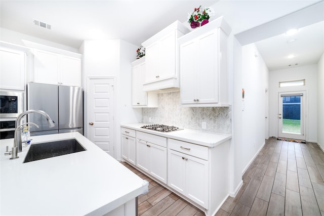 10554 Cecilia Star Ln, Richmond, TX 77406 - kitchen featuring appliances with stainless steel finishes, a sink, light wood-style floors, decorative backsplash, and white cabinets