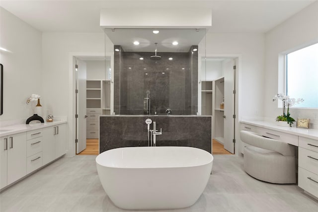 bathroom featuring a walk in closet, a freestanding tub, tiled shower, and vanity