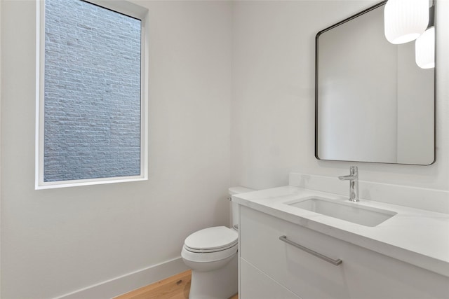 half bathroom featuring baseboards, wood finished floors, toilet, and vanity
