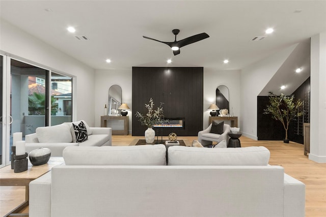 living room with arched walkways, light wood-style flooring, ceiling fan, a fireplace, and visible vents