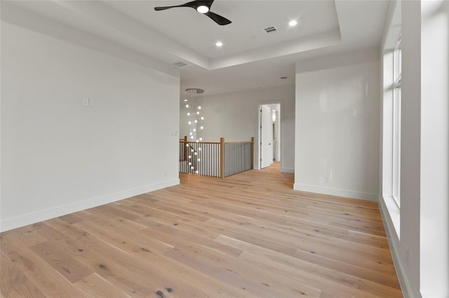 empty room with ceiling fan, light wood-style floors, a tray ceiling, baseboards, and recessed lighting