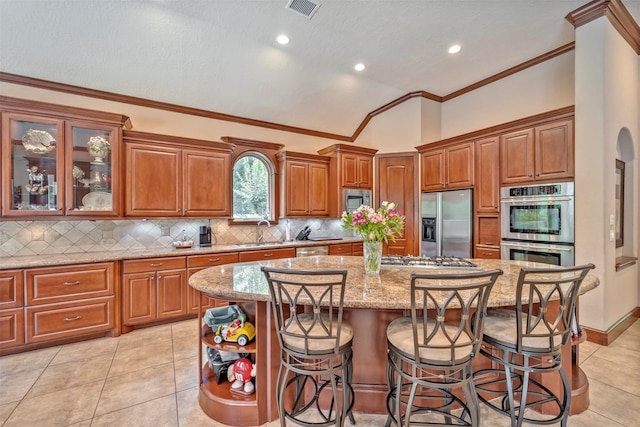 kitchen featuring light stone countertops, stainless steel appliances, a kitchen island, brown cabinets, and a sink