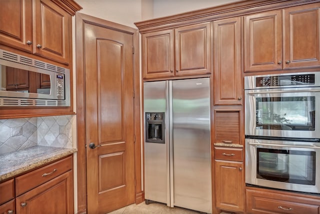 kitchen with stainless steel appliances, brown cabinets, decorative backsplash, and light stone counters