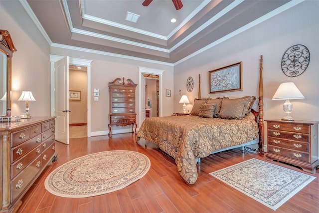 bedroom featuring wood finished floors, ornamental molding, ceiling fan, visible vents, and a tray ceiling