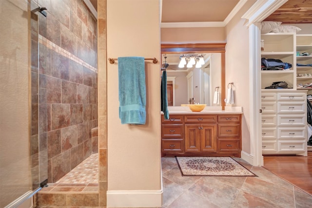 bathroom with a tile shower, vanity, baseboards, ornamental molding, and a spacious closet