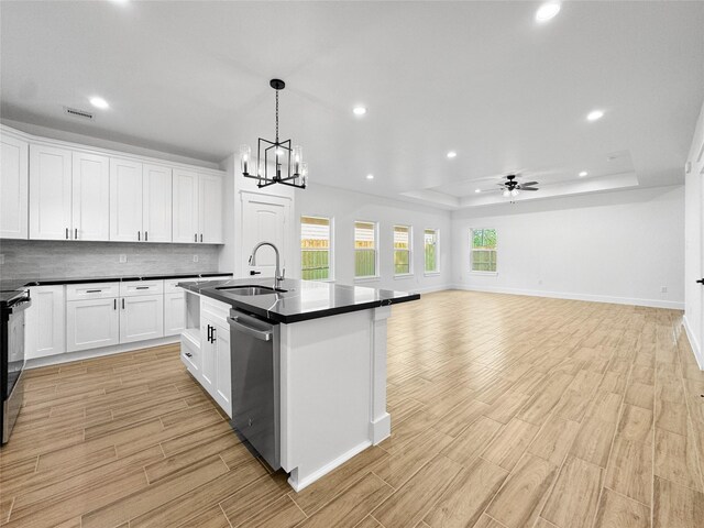 kitchen featuring recessed lighting, stainless steel dishwasher, light wood-style flooring, dark countertops, and a sink