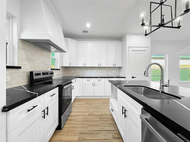 kitchen with a chandelier, appliances with stainless steel finishes, white cabinets, a sink, and premium range hood