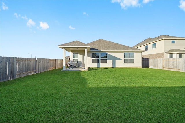 rear view of property featuring a fenced backyard, a shingled roof, a yard, and a patio area