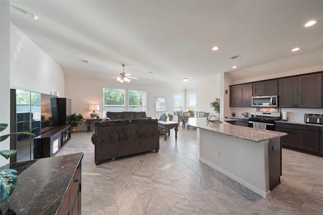 kitchen with light stone countertops, dark brown cabinets, a wealth of natural light, and appliances with stainless steel finishes
