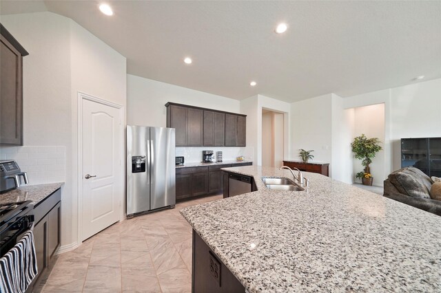 kitchen featuring light stone counters, a sink, stainless steel appliances, dark brown cabinetry, and recessed lighting