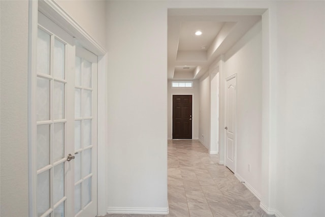 corridor with recessed lighting, a raised ceiling, marble finish floor, baseboards, and french doors