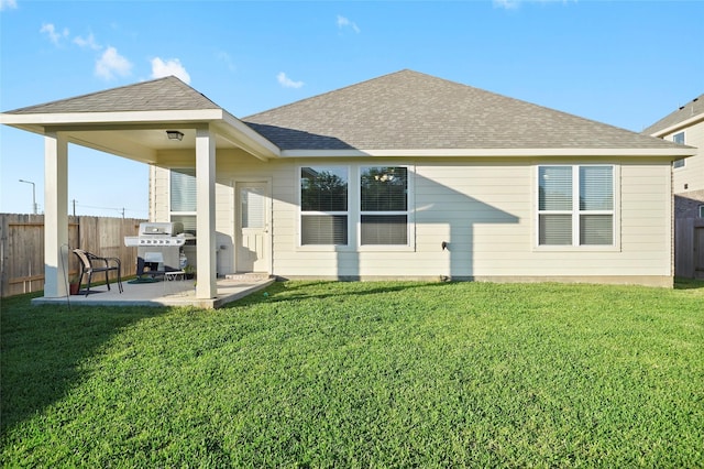 back of house with a patio, roof with shingles, a yard, and fence