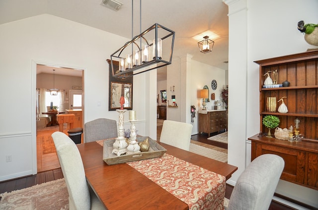 dining space featuring lofted ceiling, visible vents, a chandelier, decorative columns, and wood finished floors