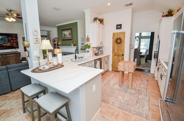 kitchen featuring a sink, a ceiling fan, visible vents, white cabinetry, and a peninsula