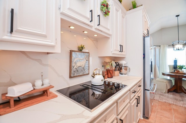 kitchen featuring light stone countertops, black electric stovetop, decorative light fixtures, white cabinetry, and freestanding refrigerator