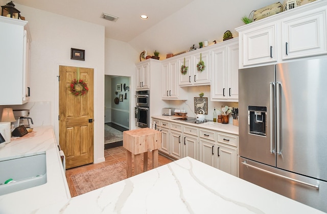 kitchen with stainless steel appliances, white cabinets, visible vents, light tile patterned flooring, and lofted ceiling