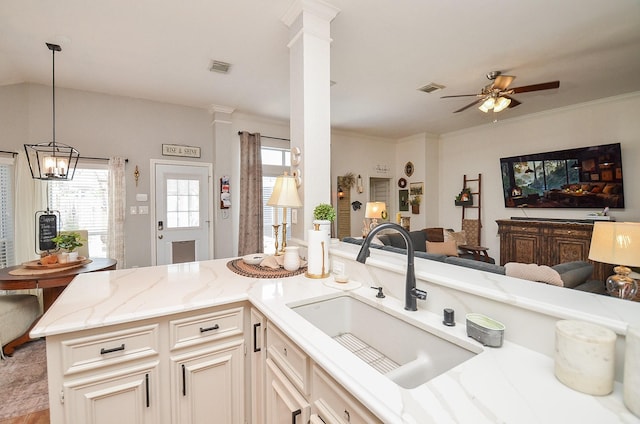 kitchen with light stone countertops, ceiling fan with notable chandelier, a sink, visible vents, and open floor plan