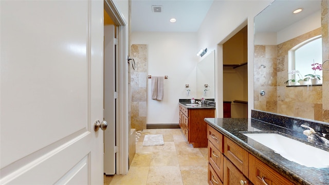 full bathroom with a walk in closet, two vanities, a tile shower, and a sink